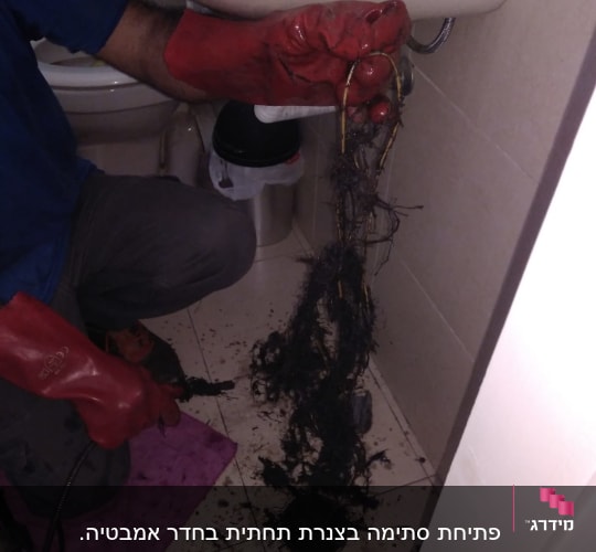 אינסטלטור עם כפפות אדומות מנקה סתימה בכיור
